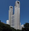 Ground-level view of a grey, window-dotted high-rise; as the building rises, two towers break off on both sides