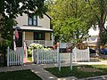 Pale yellow wooden house with brown trim surrounded by white picket fence