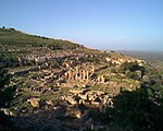 A picture of a demolished city, located on a cliff looking out to the right. A relatively larger building's beams in the middle of the city continue to stand without a roof.