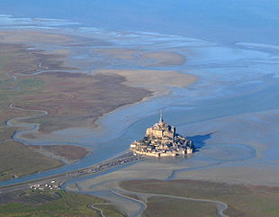 The surroundings of Mont Saint-Michel at low tide. While windy coasts are good locations for wind farms, aesthetic considerations may preclude such developments in order to preserve historic views of cultural sites. MtStMichel avion.jpg