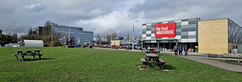 Greenspace with picnic benches with a backdrop of shops and offices