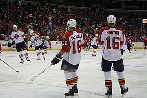 Two hockey players stand on the ice during pregame warm-up with their backs to the camera