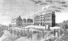Black and white image of a smaller building on the left and a larger building on the right with a courtyard in between, surrounded by trees