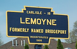 A keystone shaped road marker containing the distance to Carlisle of 18 miles, the name Lemoyne, the description of formerly named Bridgeport, and incorporated 1905.