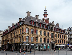 Photo de la Vieille Bourse vue depuis la place du Général-de-Gaulle avec deux lignes de douze fenêtres dont une plus grande au milieu, sur le toit dix lucarnes et un campanile. Au rez-de-chaussée se trouvent au milieu l'une des portes d'entrée, ainsi que plusieurs enseignes modernes.