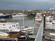 small boats lined up in harbour. Crane in the background & metal walkway in the foreground.