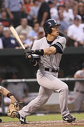 left-handed baseball player wearing a grey baseball uniform looks to the right as he follows through a swing with his bat.