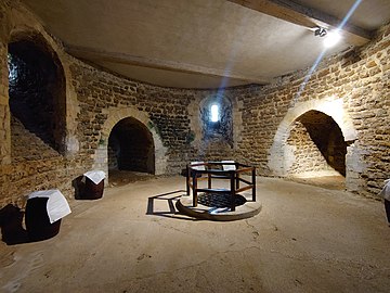A room lit by an electric light. There is a circular hole in the floor surrounded by a wooden fence marking the well.