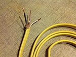 A photo of NM cable with a stripped end and a yellow colored PVC sheath.