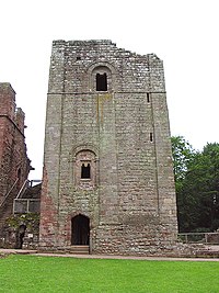 A square stone keep dominates the picture, sat behind a patch of green grass; the keep has a doorway at ground level, with two windows irregularly placed above it.