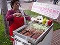 Street food vendor in Los Angeles, she is serving a popular style of bacon-wrapped hot dog served outside sporting events in the LA area.