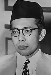 A man in spectacles and a songkok, looking left