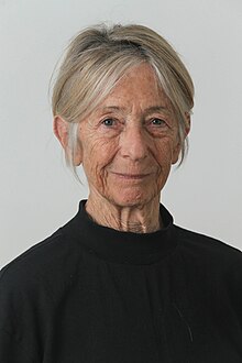 Photographic head-and-shoulders portrait of Iris Stern Levi; she is looking into the camera, wearing a sleeveless black blouse, and she has short-to-medium length straight, graying blonde hair.