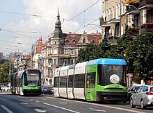 Zdjęcie. Niskopodłogowe tramwaje Pesa Swing 120NaS2 mijają się na ulicy Bolesława Krzywoustego. Na drugim planie drzewa osłaniające kamienice.