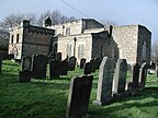 In the background is a small stone church building. In the foreground is a graveyard.