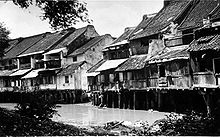 Two story houses supported by pillars stand along the riverside.