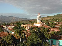 A group of buildings with red roofs in the middle of green trees and hills. There is a taller building with a tower in the center.