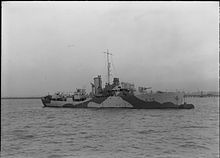 ship at sea steaming from left to right, her guns are unmanned and the bridge crew can be seen