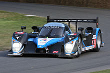 Voiture d'endurance noire et bleu azur, vue de trois-quarts, à la sortie d'un virage.