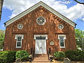 The main façade of a brick church with white double doors and a round window in the façade's gable