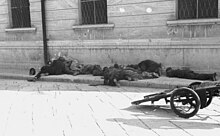 Image en noir et blanc d'un corps d'hommes en uniforme sur un trottoir et d'un canon d'artillerie