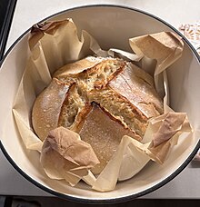 A freshly baked homemade sourdough boule within a cast iron dutch oven