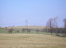 V popředí se nachází posekané pole, jež je vzadu ohraničeno vzrostlými stromy od louky. V pozadí stoupá Mořkovský vrch, na kterém ve základnová stanice mobilního operátora a stožáry vysokého elektrického napětí.