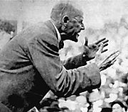 Older man in suit hectoring a crowd