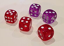 Five six-sided dice on a surface; the dice display various numbers with white pips. The three in the front of the image are red dice and behind them are two purple dice.