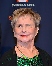 A woman, standing, wearing a green necklace.