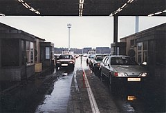 Photographie de deux lignes de véhicules passant entre deux bâtiments sous un toit de tôles. Quatre cabines de contrôle des passeports sont visibles. Les lignes de véhicules de prolongent à l'arrière-plan et l'on peut voir une tour équipée de projecteurs.