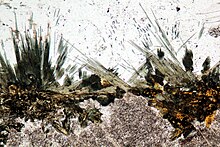 Thin section of luxullianite from Cornwall, showing clusters of radially-arranged, acicular, greenish tourmaline crystals Luxullianite rock.JPG