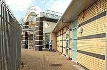 Narrow, bright alleyway, leading to a modern arched entrance of a single-floor, brick-built building.