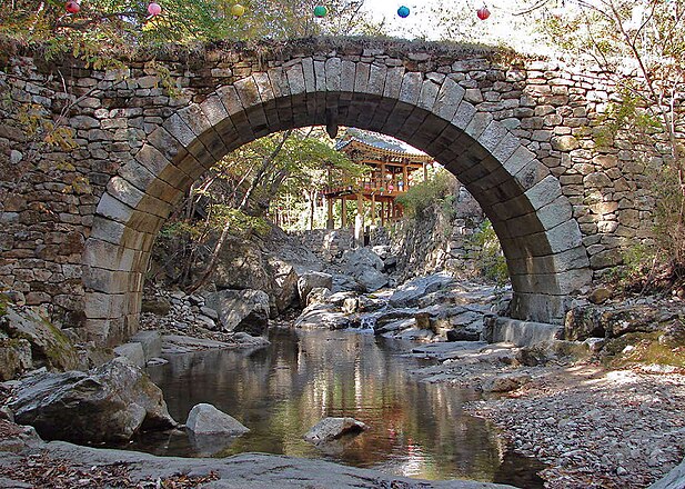 Seungseongyo, or Seungseon Bridge, is a granite stone bridge constructed in semi-circular arch configuration 14 m./46 ft long and 3.5 m./11.5 ft. wide. Monk Hoan built this Joseon Era bridge over a period of six years beginning in 1713. Through the bridge, one can see Seonam Temple, Seonamsa, a Korean Buddhist temple located on the eastern slope at the west end of Mount Jogyesan Provincial Park, in the city of Suncheon, Jeollanamdo Province, South Korea. Photo by Steve46814, October 2011.