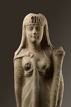 Marble statue depicting a woman facing forward. She wears a diadem on her head with a triple uraeus (three snakes) on it. Inscribed on her right arm is a cartouche, and she holds a cornucopia in her left arm.