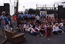 Women sitting on ground to block gates which have a line of police in them