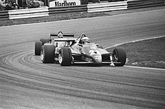 Black-and-white photograph of two racing cars going through a corner