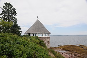 view of circular bathhouse, with trees and greenery in foreground and ocean and beach in the background