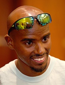 Mo Farah with a white t-shirt and tinted sunglasses on his head.