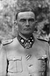 A man wearing a military uniform and neck order in the shape of a cross. His hair is combed back and his facial expression is determined.