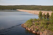 Un grand barrage retenant un lac, entouré de forêts.