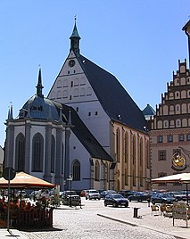 Barevná fotografie s pohledem na štít hlavní obdélníkové lodi kostela se sanktusníkem a přístavbou v podobě kaple