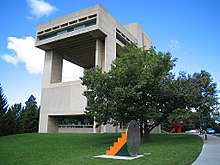 Un bâtiment moderne aux formes rectilignes, reposant sur de vastes piliers et installé au milieu d'une zone de verdure.