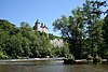 Gevels en daken tussen de twee ronde torens rechts van de rotswand van het kasteel van Walzin, en de gevels en daken van de toren genaamd "15ème siècle" en het ensemble van het kasteel van Walzin, de rots "Al penne" met zijn ruïnes van Caverenne, en het bos La Lesse en een dee van de alluviale vlakte