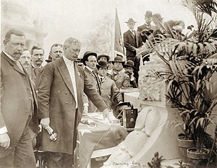 Photographie sépia d'un homme entouré d'une foule appuyant sur un bouton