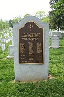 A tall stone monument stands on a grassy hill in a graveyard