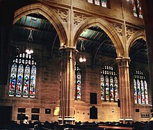 View across the nave of St. Andrew's shows the arches supported on tall clustered columns, and with spandrels decorated with quatrefoil tracery. The four-light Perpendicular aisle windows are full of red, blue and purple figurative stained glass