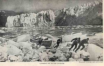 Six men pulling a boat on to an icy shore, with a line of ice cliffs in the background