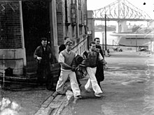 Black and white photograph of five men walking out of a building