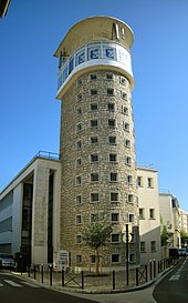 Une haute tour en pierre situé en angle d'une rue.
